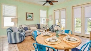 A dining area with a round wooden table, blue chairs, and a ceiling fan. - Kiva's Jewel - Guest House (Gulf Shores)