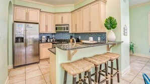 A kitchen with a refrigerator, microwave, and a bar area with stools. - Kiva's Jewel - Guest House (Gulf Shores)