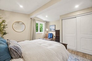 A bedroom with a bed, a chair, a desk, a wardrobe, a mirror, and a window with curtains. - Pet-Friendly 1BR With Office & Fenced Yard (Ottawa)