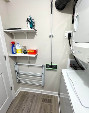 A laundry room with a washing machine, shelves with cleaning supplies, a drying rack, and a mop. - Pet-Friendly 1BR With Office & Fenced Yard (Ottawa)