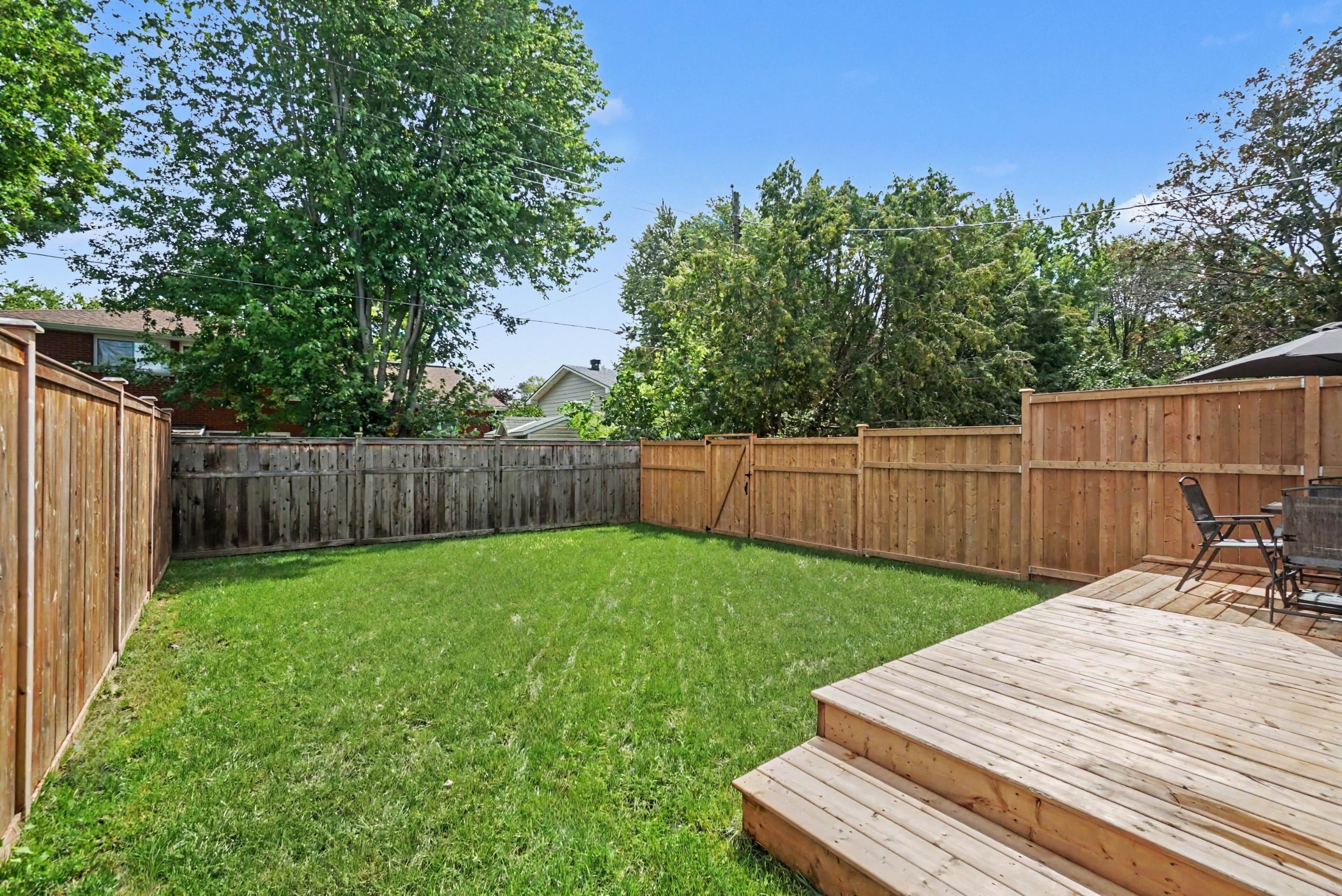 Un jardin avec une terrasse en bois, une pelouse et une clôture en bois.