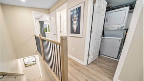A hallway with a wooden staircase, a door with a decorative mirror, and a kitchen area with appliances. - Pet-Friendly 1BR With Office & Fenced Yard (Ottawa)
