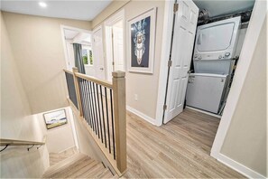 A hallway with a wooden staircase, a door with a decorative mirror, and a kitchen area with appliances.