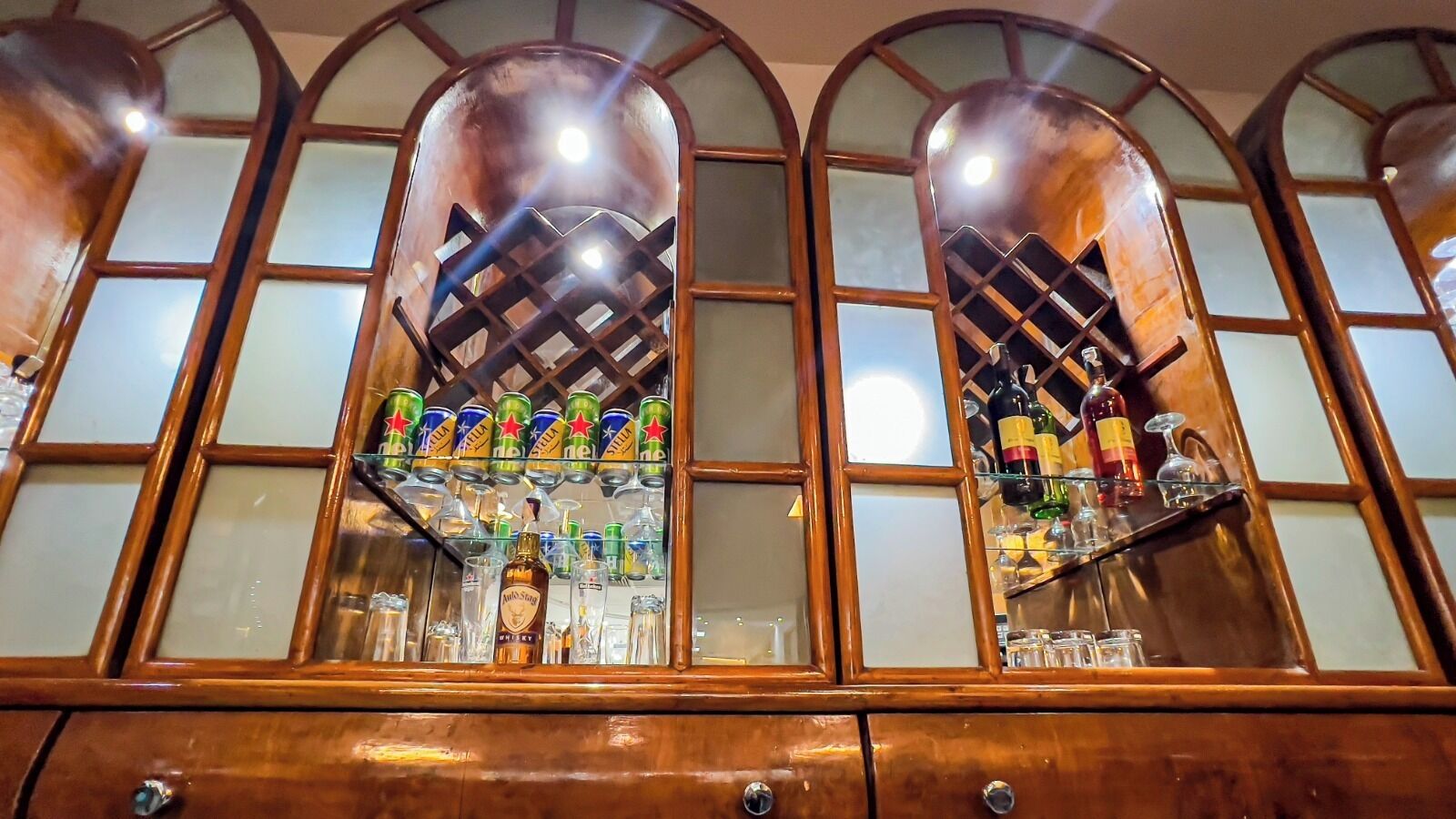 A bar area with a wooden cabinet, shelves with liquor bottles, and a display of canned beverages.