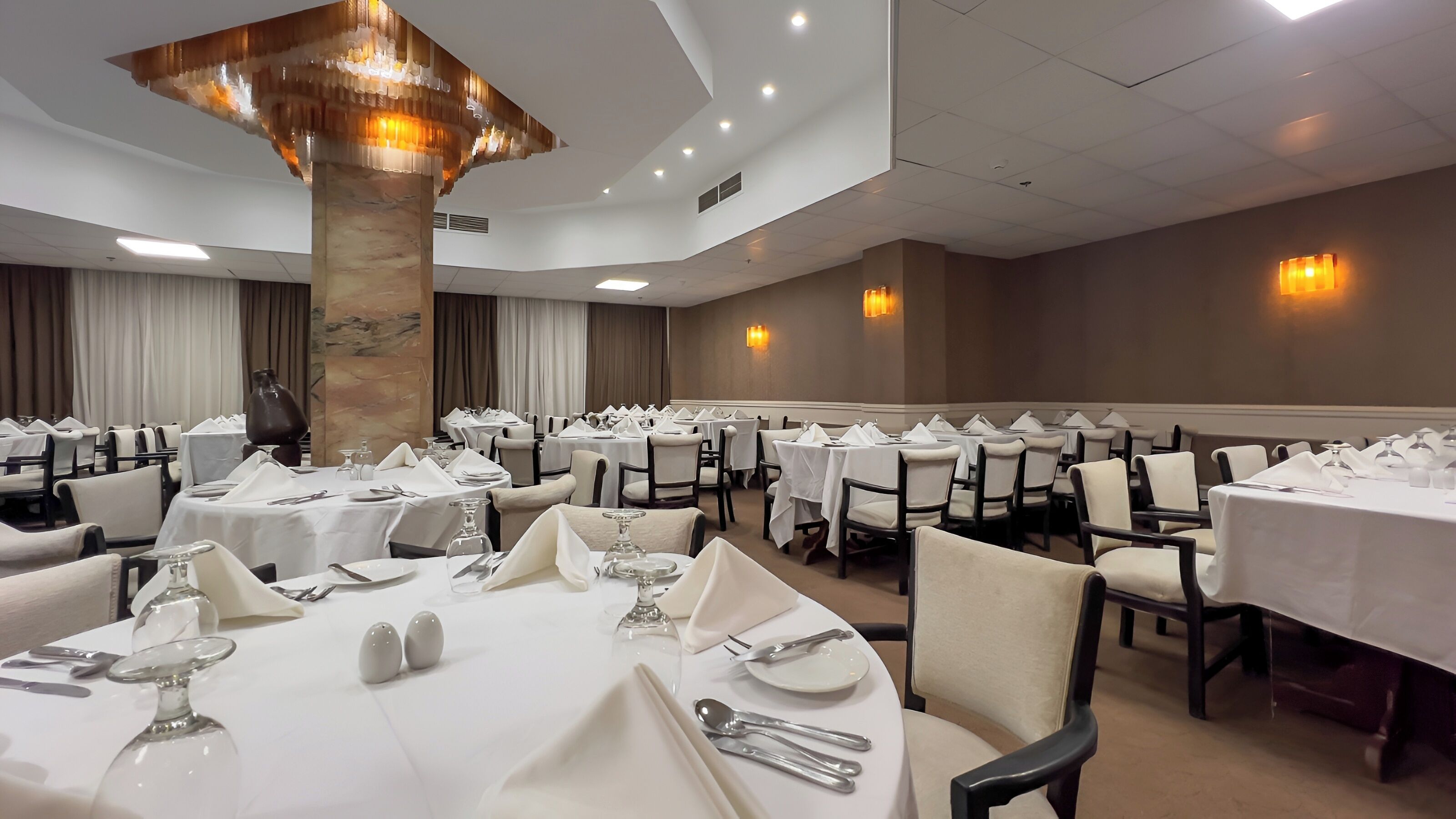 A banquet hall with round tables set for dining, featuring white tablecloths, silverware, and glassware.