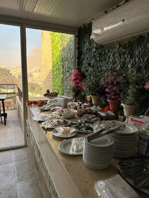 A kitchen with a view of pyramids, a counter with food items, and a wall with artificial plants. - Sahary Pyramids View Hotel (Giza)