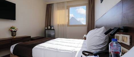 A hotel room with a bed, bedside table, lamp, and a window with a mountain view.