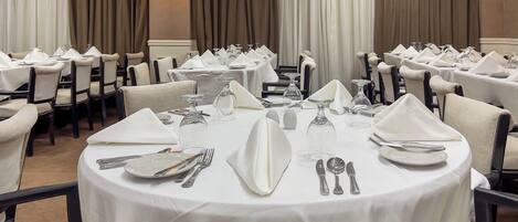 A banquet hall with round tables set for dining, featuring white tablecloths, silverware, and glassware.
