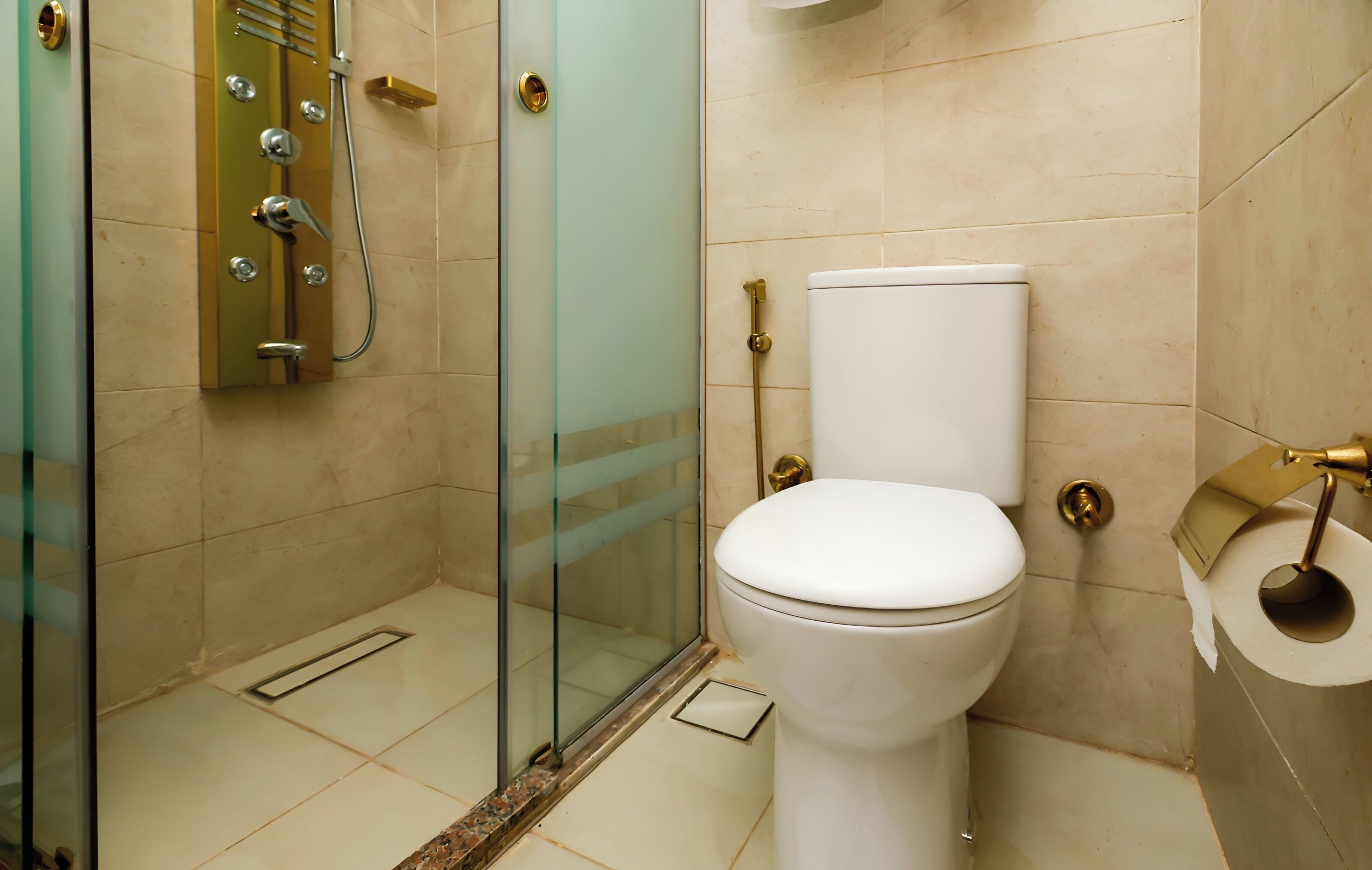 Un baño moderno con ducha envuelta en vidrio, inodoro blanco y grifo con detalles dorados.