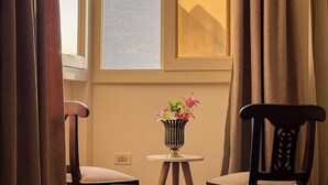 Een kamer met uitzicht op een berg, een vaas met bloemen op een bijzettafeltje, en twee stoelen.