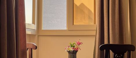 A room with a view of a mountain, a vase with flowers on a small table, and two chairs.