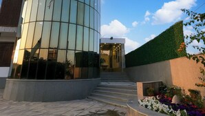 Een modern gebouw met een glazen gevel, een trap die naar een ingang leidt, en een aangelegde tuin met bloemen.