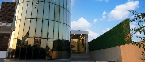 Un edificio moderno con fachada de vidrio, una escalera que lleva a la entrada y una zona ajardinada con flores.