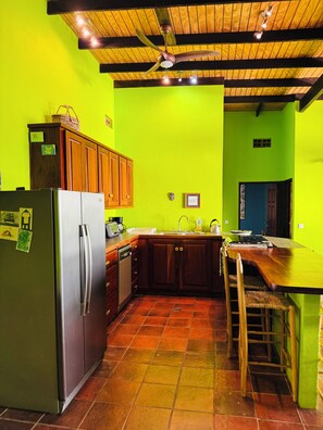 A kitchen with a green wall, wooden cabinets, a stainless steel refrigerator, and a wooden ceiling with exposed beams.