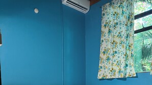Una habitación con dos camas de madera, una pared azul, una ventana con cortinas florales y un piso de baldosas.