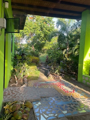 A pathway leading through a lush garden with a mosaic-tiled floor and a variety of tropical plants.