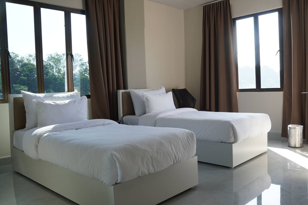 A modern hotel room with two beds, large windows, and a view of the outdoors.