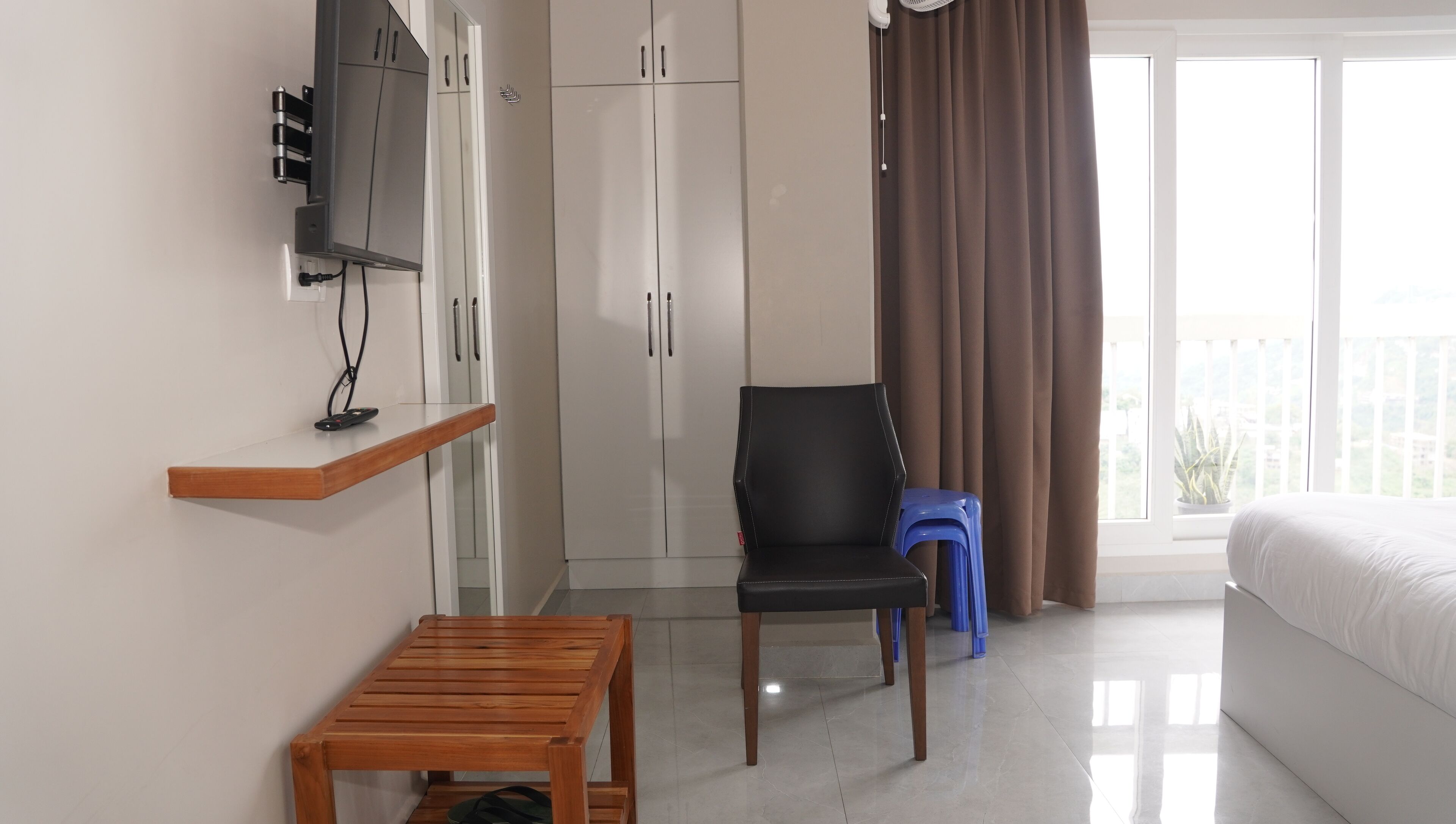 A hotel room with a bed, a desk, a chair, a wardrobe, and a balcony with curtains.