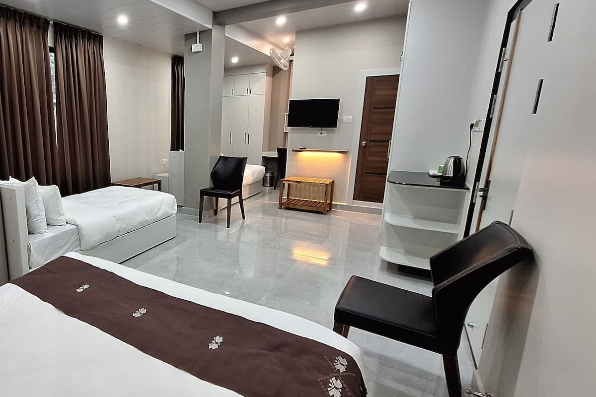 A modern hotel room with a bed, a desk, a chair, a TV, and a small table with a kettle.