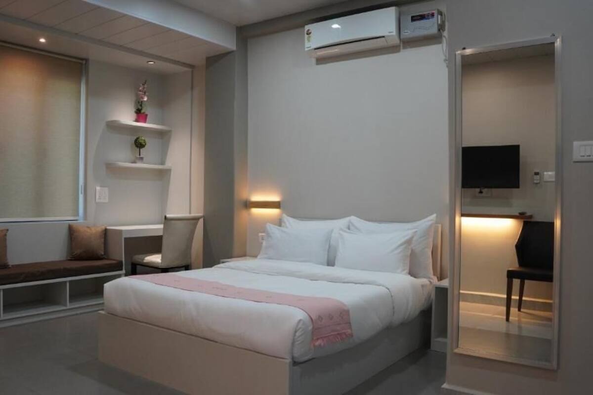 A modern bedroom with a bed, bedside tables, a chair, a bench, and a TV.