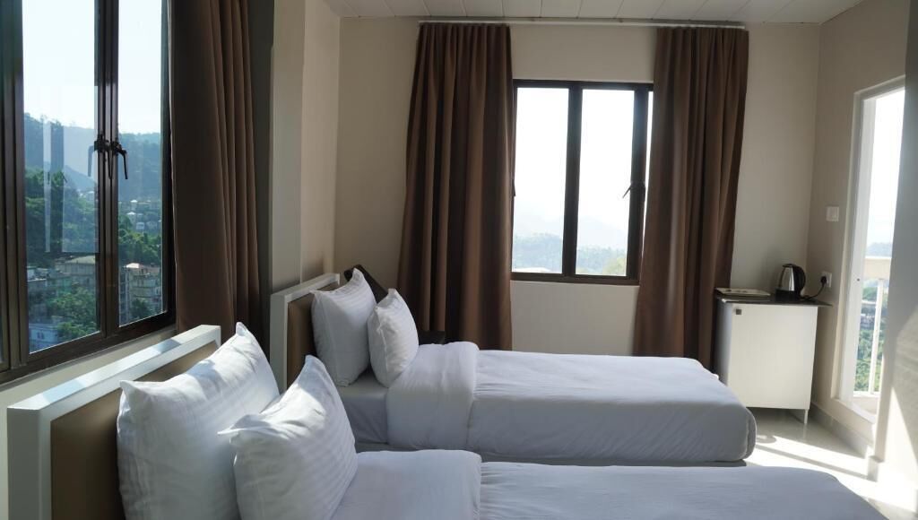 A hotel room with two beds, a desk, and a window with curtains.