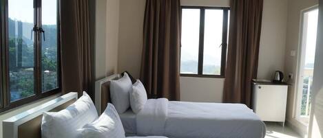 A hotel room with two beds, a desk, and a window with curtains.