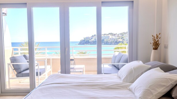 Une chambre avec un grand lit, une vue sur la mer et un balcon aménagé avec des sièges.