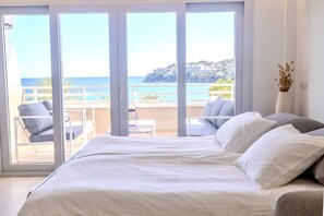 Une chambre avec un grand lit, une vue sur la mer et un balcon aménagé avec des sièges.