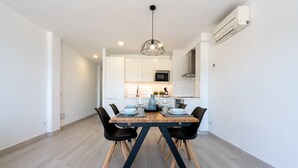 Un espace repas moderne avec une table en bois et des chaises noires, un luminaire suspendu et une cuisine en arrière-plan.
