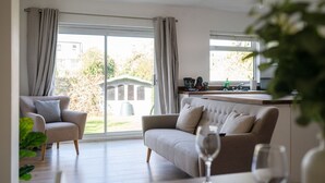 Ett modernt vardagsrum med en soffa och en fåtölj, en matplats med ett bord och stolar samt en köksbänk med en diskho och ett fönster.