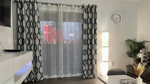 Un salon moderne doté d’une grande fenêtre, d’un téléviseur à écran plat fixé au mur, d’un canapé, d’une table basse et d’une plante en pot.