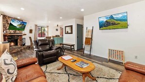 A living room with a fireplace, leather sofa, wooden coffee table, and a painting of a landscape. - Slopeside Cabin C W Hot Tub & Slope View Parking (Big Bear Lake)