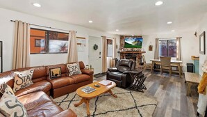 A living room with a brown leather sofa, a wooden coffee table, and a TV in the background. - Slopeside Cabin C W Hot Tub & Slope View Parking (Big Bear Lake)