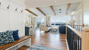 A spacious living area with a wooden bench, a sofa, and a dining table. There is a staircase with a wooden railing leading to an upper level. - Design-forward Lake Views Bay Harbor (Petoskey)