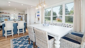 A modern kitchen with white cabinetry, a central island with bar stools, and a large window offering a view of the outdoors. - Design-forward Lake Views Bay Harbor (Petoskey)