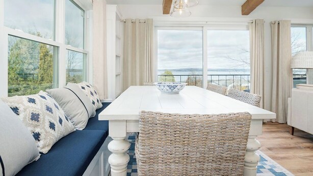 A dining area with a white table, wicker chairs, and a blue sofa with patterned cushions. - Design-forward Lake Views Bay Harbor (Petoskey)