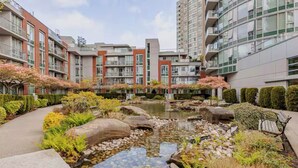 Un moderno complejo de apartamentos con un patio central que cuenta con un pequeño estanque, rodeado de follaje cuidado y senderos de piedra.