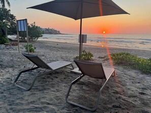 Two sun loungers with a beach umbrella on a sandy beach with a sunset in the background. - Luxury Oceanfront At Majahua (La Majahua)