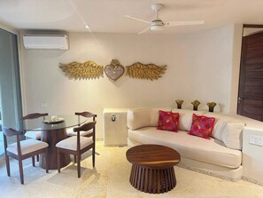 A living room with a glass-top table, wooden chairs, a sofa with colorful cushions, and decorative wall art. - Luxury Oceanfront At Majahua (La Majahua)