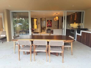 A dining area with a large wooden table and wicker chairs, a kitchen with dark cabinets, and a sliding glass door leading to an outdoor area. - Luxury Oceanfront At Majahua (La Majahua)