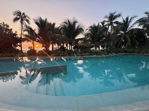 A clear swimming pool surrounded by palm trees and a sunset in the background. - Luxury Oceanfront At Majahua (La Majahua)