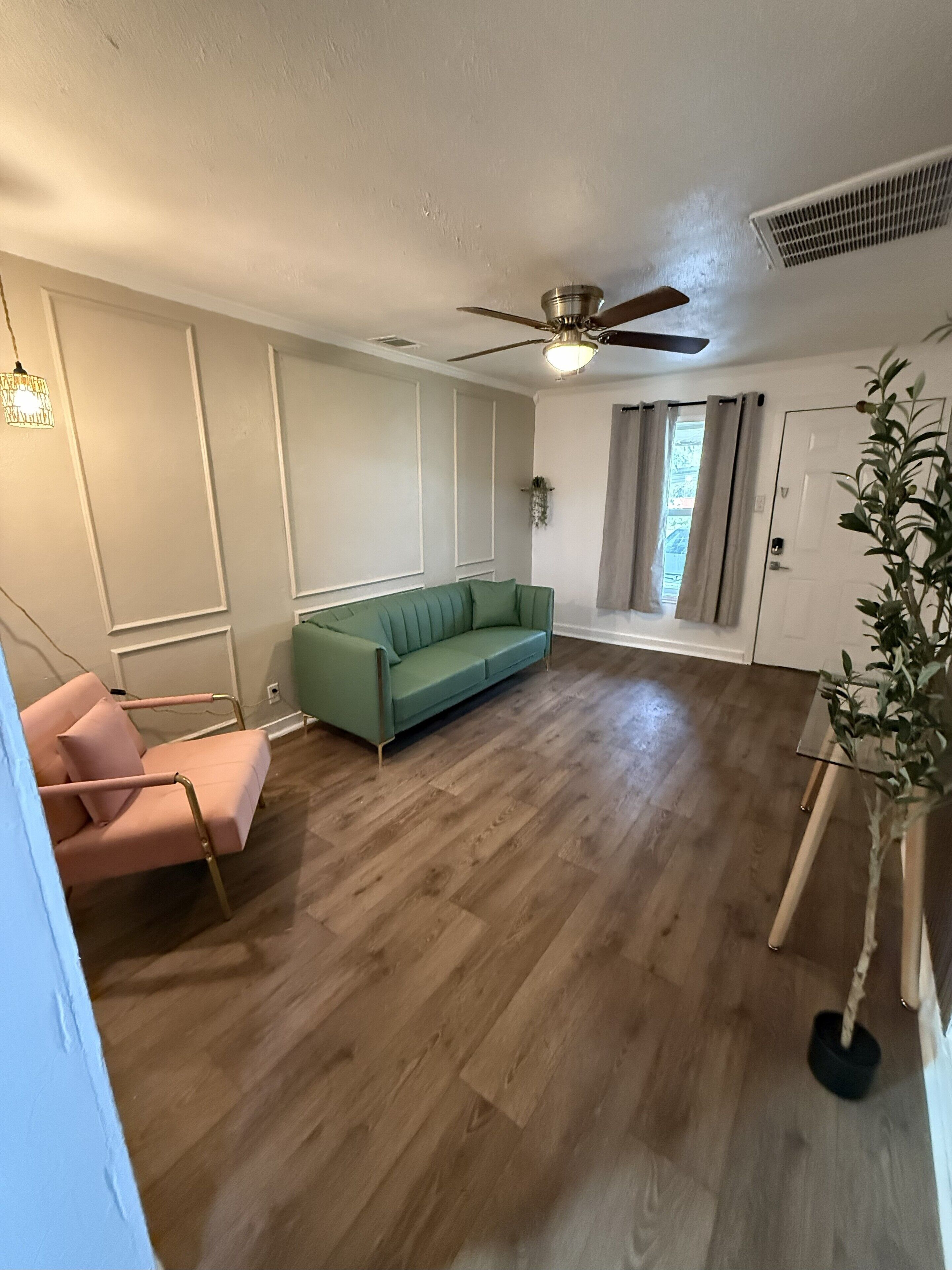 Een ruime woonkamer met een groene bank, een roze fauteuil en een plafondventilator.