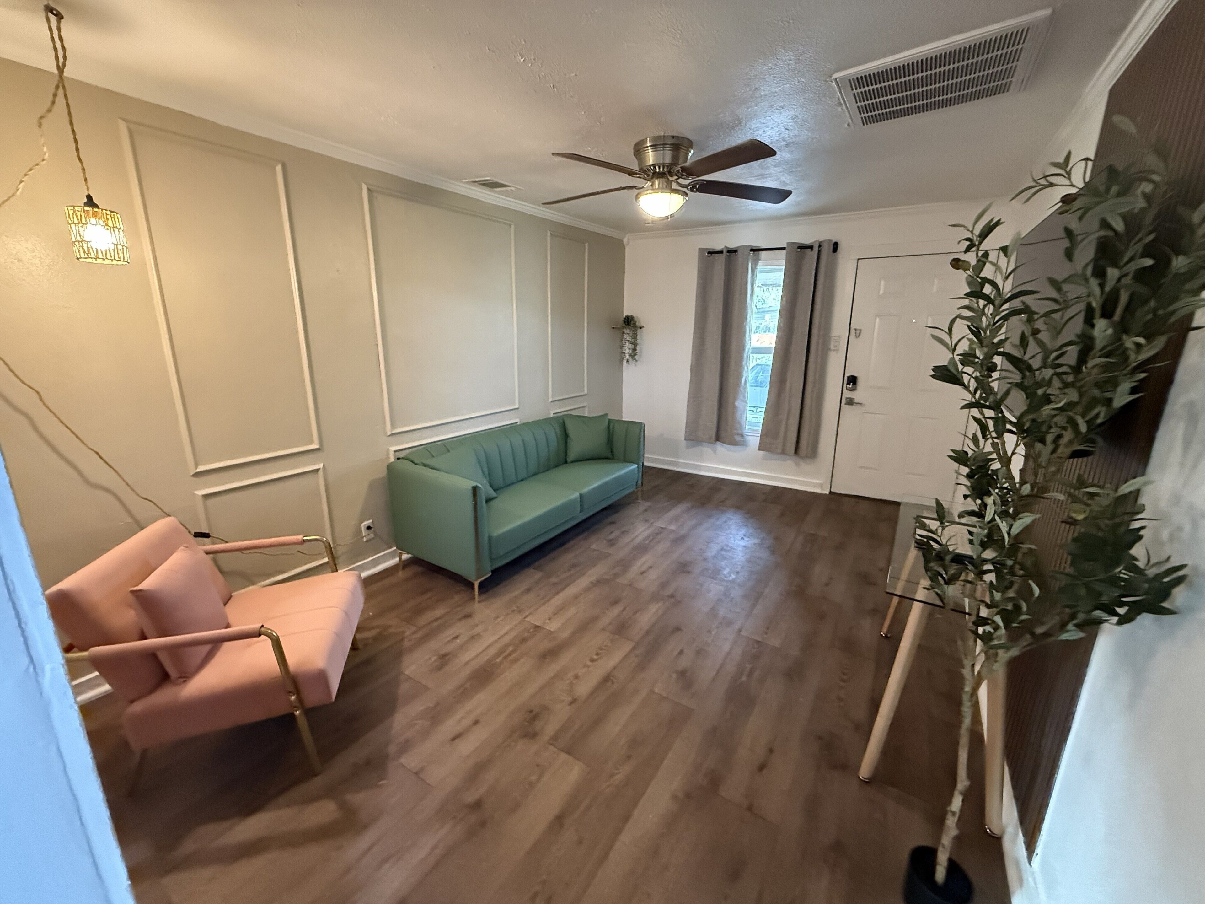 A spacious living room with a green sofa, a pink chair, a ceiling fan, and a potted plant.