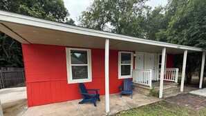 A red building with a covered porch, two blue Adirondack chairs, and a white fence. - 1BR Minutes to Stockyards • Fast Wi-Fi + Parking (Fort Worth)