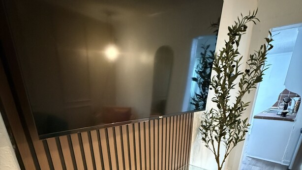 A modern interior with a large flat-screen TV mounted on a wall, a wooden bench with a placard, and a potted plant. - 1BR Minutes to Stockyards • Fast Wi-Fi + Parking (Fort Worth)