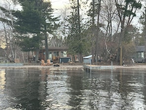 Una cabaña junto al lago con un muelle, rodeada de árboles y un cobertizo pequeño.
