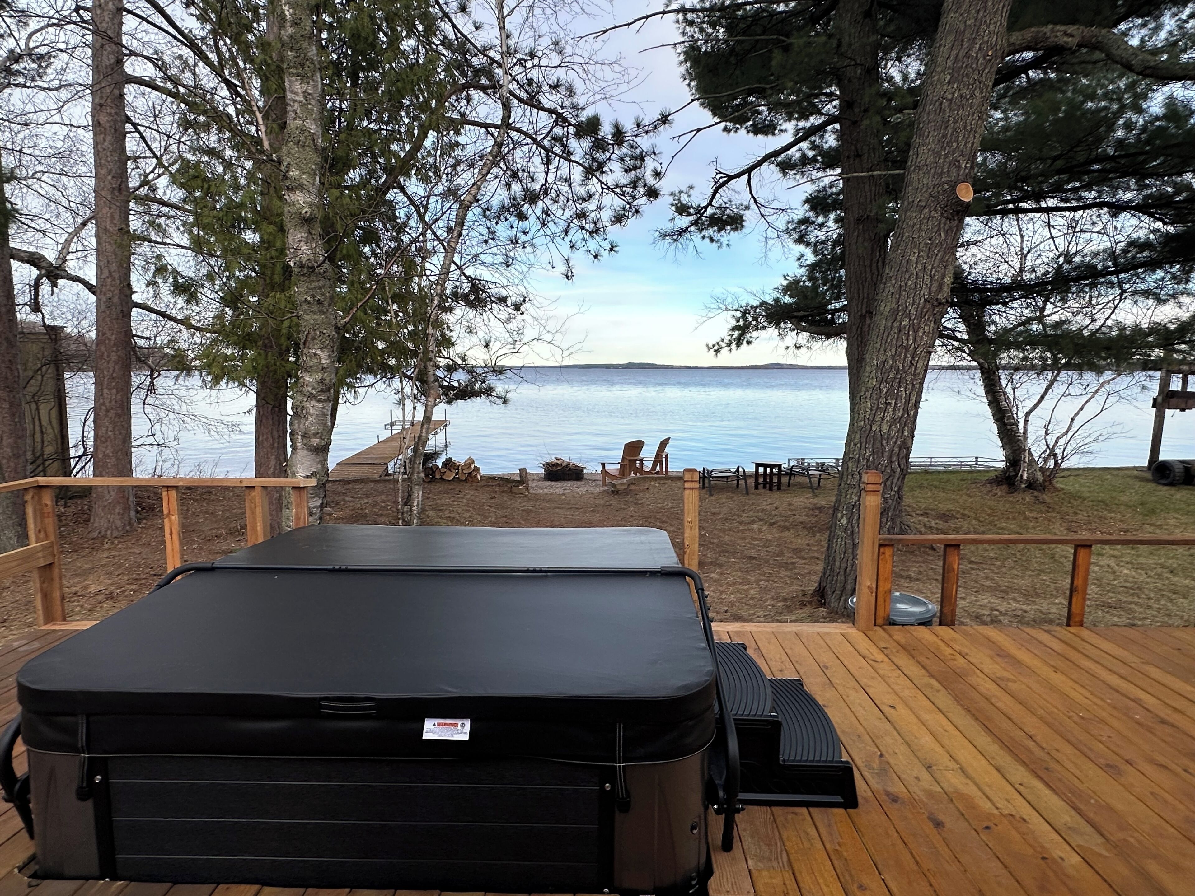 A deck with a hot tub, wooden railings, and a view of a lake.