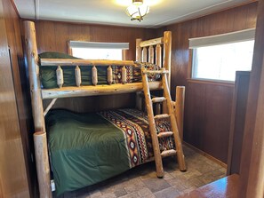 Una cama litera con escalera, paredes de madera y una ventana.
