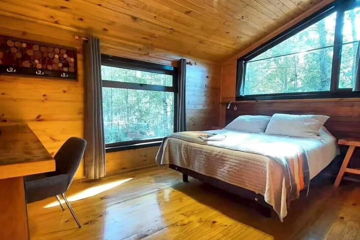 A wooden cabin bedroom with a bed, a desk, and a chair.