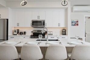 Een moderne keuken met witte kastjes, een centraal eiland met zitplaatsen, een magnetron en een broodrooster.